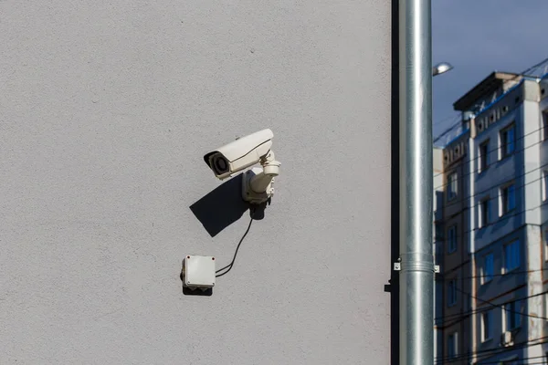 Mała biała kamera monitoringu na płaskiej szarej, matowej ścianie tynku w mieście — Zdjęcie stockowe