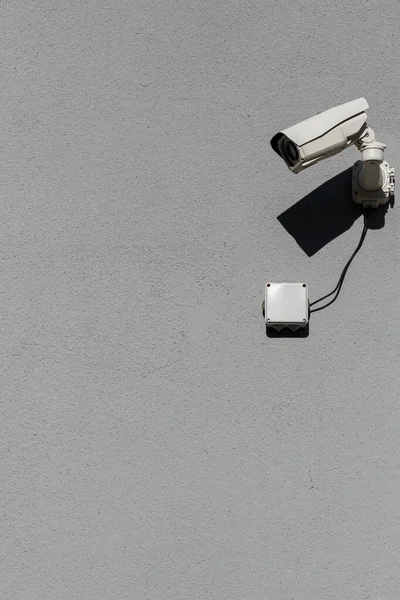 Mała biała kamera monitoringu na płaskiej szarej, matowej ścianie gipsowej — Zdjęcie stockowe