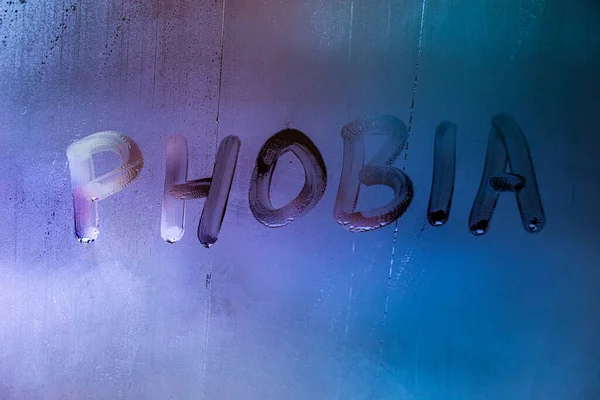 Słowo fobia odręcznie napisane na mokrej mglistej powierzchni okna z niebieskim świetle tła — Zdjęcie stockowe