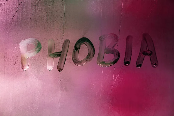 Słowo fobia odręcznie napisane na mokrej mglistej powierzchni okna z czerwonym świetle tła — Zdjęcie stockowe