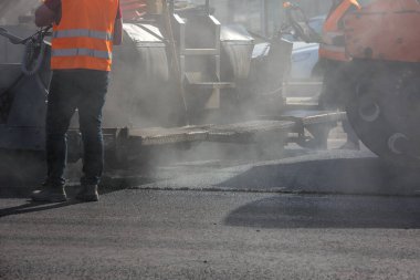 Yol boyunca asfalt kaldırma makinesiyle çalışan adamlar gün ışığında duman ve buharla tamirat yapıyorlar.