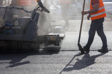 Yol boyunca asfalt kaldırma makinesiyle çalışan adamlar gün ışığında duman ve buharla tamirat yapıyorlar.