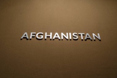 Kaba ten rengi haki rengi kumaşın üzerine gümüş metal harflerle yazılmış Afganistan kelimesi.