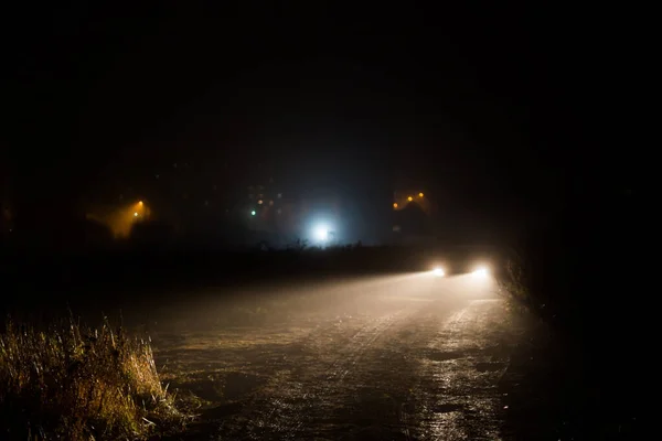 Conos de faros de coche en la niebla nocturna en el campo detrás de la ciudad — Foto de Stock