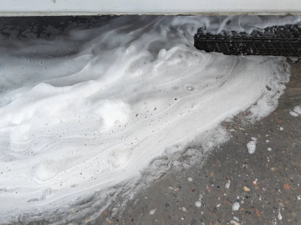 Los residuos de jabón sud fluyen a la rejilla de drenaje del suelo en el garaje de lavado de coches. Primer plano de cuadro completo con enfoque selectivo. Fotos De Stock