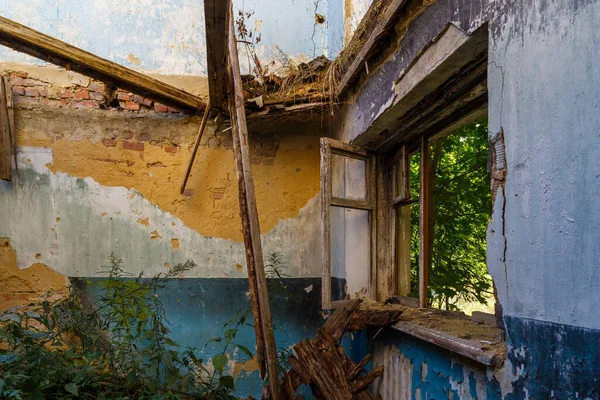 Janela de madeira quebrada e quarto com grama alta, vista para dentro de um dormitório meio destruído abandonado à luz do dia de verão — Fotografia de Stock