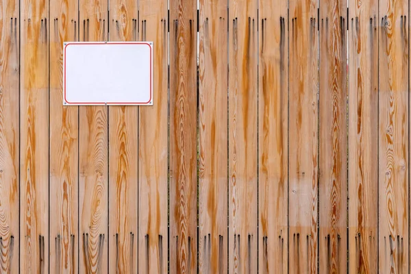 Drewniane ogrodzenie z pionowymi deskami z przykręcaną białą płytą — Zdjęcie stockowe