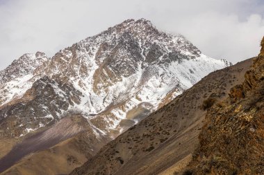 Snow-covered rocky mountains rise majestically in a vast cold landscape in Kyrgyzstan. Serene atmosphere captures the beauty of nature at high altitude during daytime.
