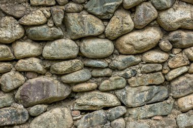 Rustic stone wall made with various sizes and shapes of round rocks, full-frame background and texture.