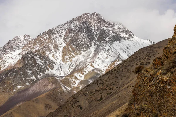 Snow-covered rocky mountains rise majestically in a vast cold landscape in Kyrgyzstan. Serene atmosphere captures the beauty of nature at high altitude during daytime.