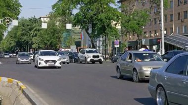 Kırgızistan, Bişkek 'te güneşli bir yaz gününde dar Asya şehir sokağında yeşil ağaçlarla kaplı arabalar geçiyor - 21 Haziran 2025