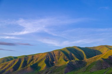 Serene mountain landscape features rolling hills under a clear blue sky in Kyrgyzstan. Tranquil outdoor setting evokes feelings of peace and calmness in nature.
