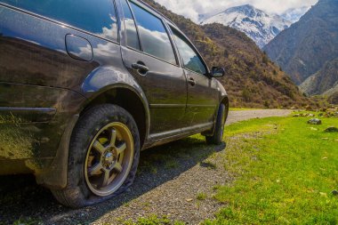 Car sits quietly with a flat tire in a desolate mountainous Kyrgyzstan area. Daytime light enhances the serene and adventurous mood of the natural landscape.