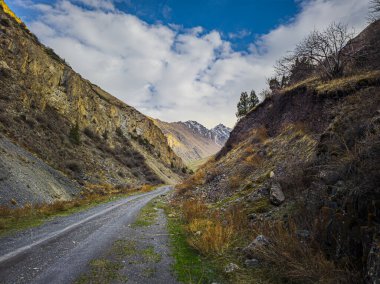 Dramatic mountain road in mountain gorge of Kyrgyzstan. Slopes are covered with dry springtime vegetation.