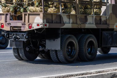 Multiple soldiers wearing camouflage uniforms sit in the back of a military truck before military parade.