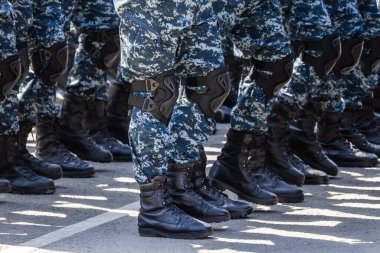 Multiple legs in urban digital camouflage pants and black boots in a daytime outdoor training area.