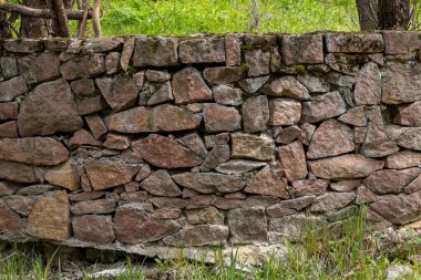 Sturdy stone wall composed of multiple rocks in various sizes and shapes. Rustic setting showcases natural beauty in a daytime outdoor environment, emphasizing the strength of nature.