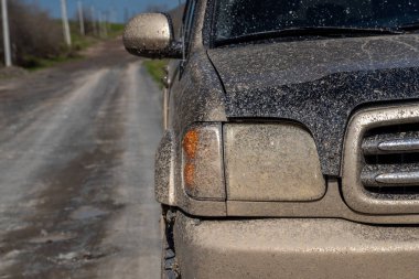 Front part of a muddy SUV parked on a gravel country road under daylight