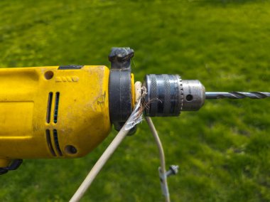 Damaged electrical wire wrapped around an old electric drill on lawn background. DIY tool safety concept.