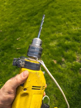 Damaged drill with a broken electrical cord is held in a grassy yard. The scene conveys feelings of neglect and wear, reflecting a state of disrepair under daylight.