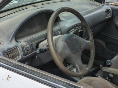 Interior of an abandoned vehicle featuring a dusty, dirty dashboard and steering wheel. Daylight reveals neglect and wear, creating a sense of solitude and abandonment.