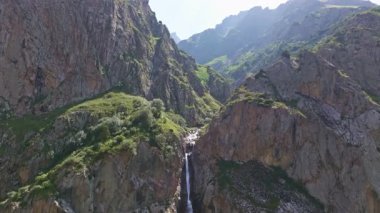 Dağlardaki dağ vadisinde küçük bir şelale güneşli yaz kırgızistan 'da hava aracı manzarası. Açık hava ve engebeli arazi. Kamera hareketini arttır.