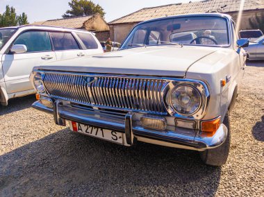 A white vintage GAZ Volga car parked on a gravel lot. The car is a classic Soviet-era vehicle, a symbol of a bygone era. Sokuluk, Kyrgyzstan - August 11, 2023