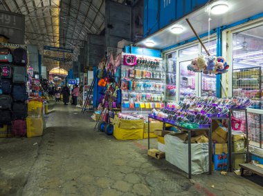 A wide shot of Junhai Market, showing vendors setting up their stalls and customers browsing the diverse goods. The market is filled with activity, with people buying and selling a variety of products. Bishkek, Kyrgyzstan - January 26, 2024