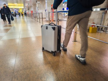 A man pushes a rolling suitcase through a brightly lit Manas airport terminal in Bishkek, Kyrgyzstan - March 2, 2024