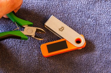 hardware Bitcoin wallet with wire cutters indoors, cold storage hacking and physical vulnerability concept