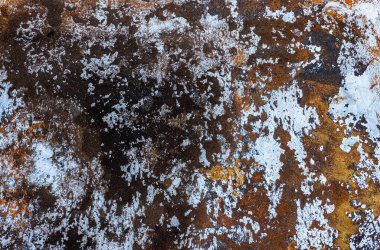 Close-up of a weathered metal surface with peeling and flaking layers of light blue and brown paint, revealing dark rusted areas.