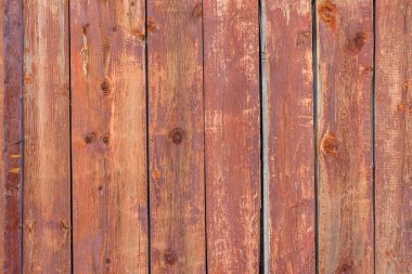 Close-up of a rustic red wooden fence with visible wood grain, knots, and signs of weathering.