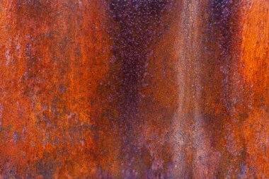 Metal surface showing a blend of orange and purple hues from rust and oxidation, with a slightly grainy texture