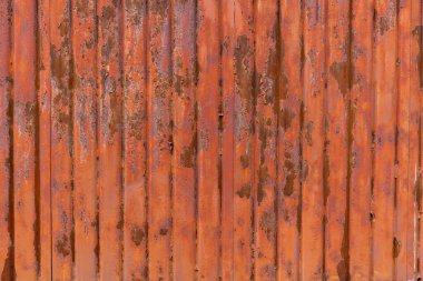 Close-up of a vertical corrugated metal sheet heavily covered in reddish-brown rust with patches of peeling paint