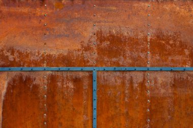 Rusty metal plates joined by blue bolted stripes. Shows aged, corroded texture and hex screw or bolt heads.