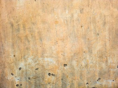 A close-up shot shows an aged beige stucco wall with a weathered surface. The grunge background reveals cracked plaster and a distressed finish, creating a textured appearance.