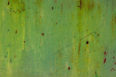 Weathered flat green metal surface displays deep scratches and rust in an industrial outdoor setting. Daylight enhances the rustic charm and aged appearance of the material.
