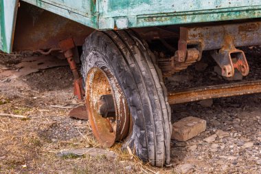 Rusty soviet trailer wheel rests on the ground. Flat tire adds to the neglected and aged mood, emphasizing wear and disrepair in the outdoors.