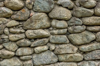 Rustic stone wall showcases various stones arranged in unique shapes and sizes. Weathered texture adds character to this outdoor scene with a tranquil mood.