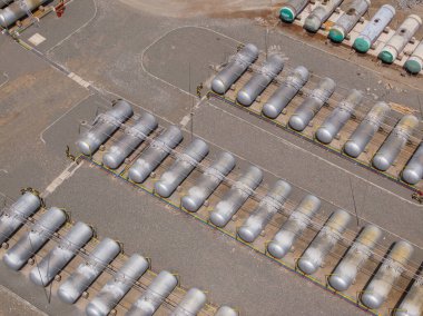 Açık mavi gökyüzünün altındaki endüstriyel bir tesiste sayısız petrol depolama tankı var. Sahne, açık hava ortamında güçlü bir faydacı tasarım ve işlevsellik hissi veriyor..