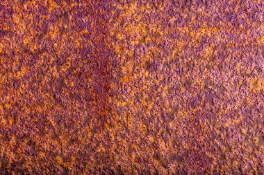 Metal surface with a thick layer of rust, exhibiting a predominantly purple hue with hints of orange and a rough texture