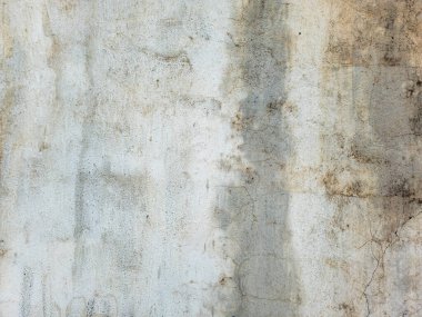 Yakın çekim, beton bir duvar dokusu, belirgin lekeler ve yıpranmış bir yüzey gösteriyor. Grunge arka planında çimentoda çizgili bir toprak ve renk değişimi var..
