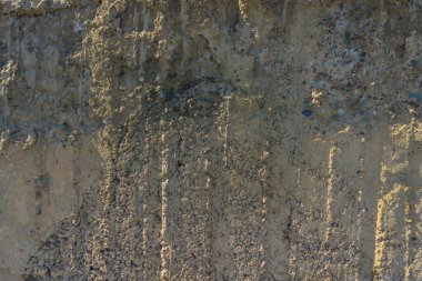Rough, uneven concrete surface embedded with small pebbles and showing signs of age and wear under tangential harsh sun light showing all imperfections.