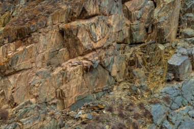 Parlak gün ışığı altında ıssız bir dağlık bölgede engebeli bir kaya oluşumu belirgin bir şekilde duruyor. Saf doğal çevre, yalnızlık ve engebeli bir güzelliğin habercisidir..