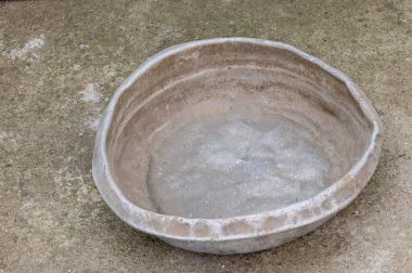 Weathered dented gray aluminum basin on concrete floor. This basin is for manual concrete mixing.