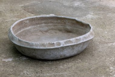Weathered dented gray aluminum basin on concrete floor. This basin is for manual concrete mixing.