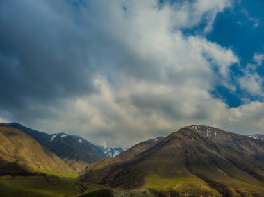 Kırgızistan 'da bahar günü, üzerinde fırtınalı bulutlar olan sakin vadideki dağların dramatik manzarası.