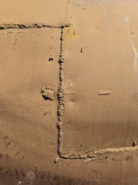 Sert, yıpranmış metal yüzey gösterileri parlak gün ışığında kaynakların karmaşıklığını gösteriyor. Endüstriyel atmosfer işçiliği ve açık hava unsurlarını hiç insan olmadan ön plana çıkarıyor.