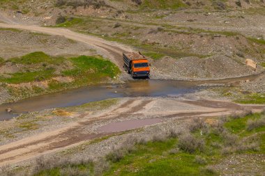 Truck loaded with rocks driving through stream in rural mountainous area. Construction material mining - is a small local business.