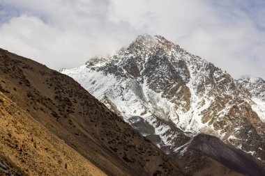 Kırgızistan 'da karla kaplı dağ zirvesi gri bulutlu gökyüzüne karşı görkemli bir şekilde yükseliyor. Rocky yamaçları bu güzel dağlık bölgede geniş ve sakin bir atmosfer yaratır..